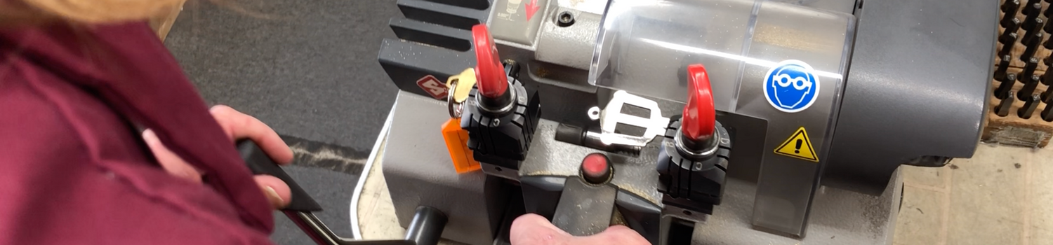A man wearing a red shirt using a manual machine to engrave a house key