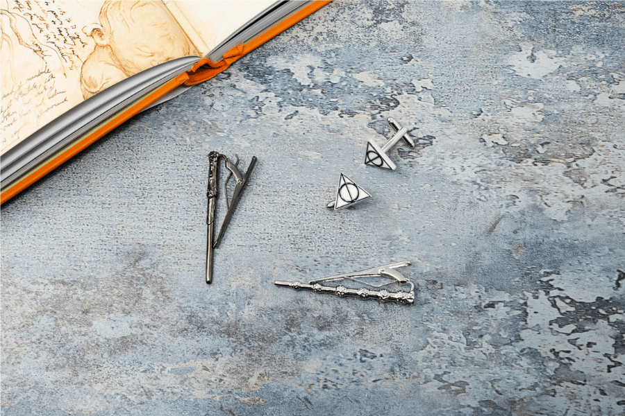 Several tie clips and cufflinks inspired by the Harry Potter series next to an illustrated copy of a Harry Potter book