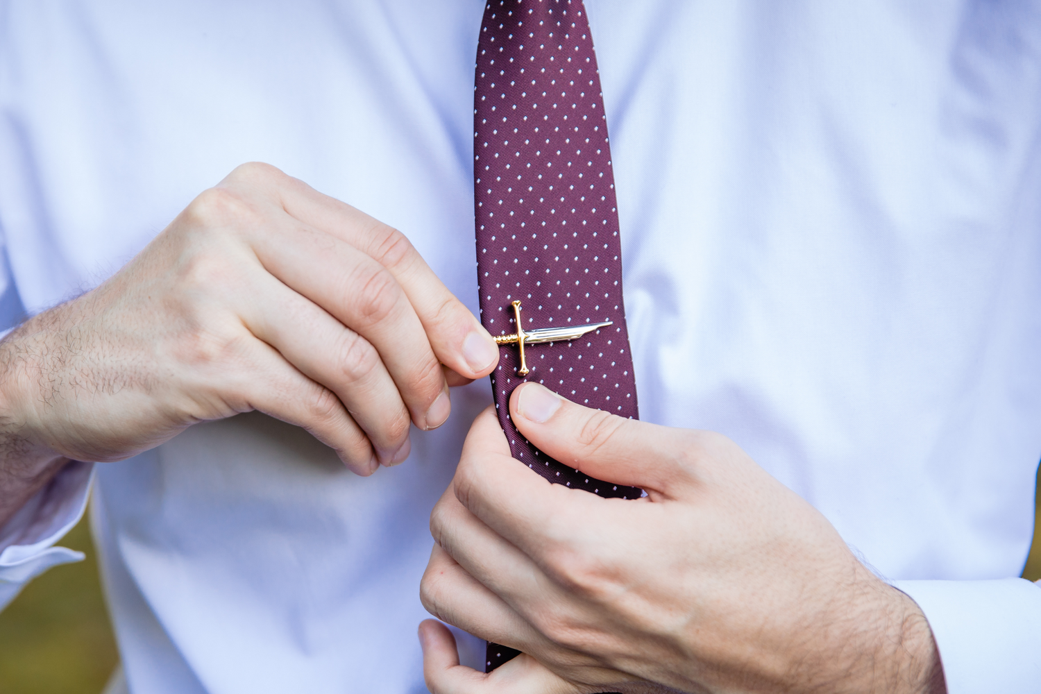 A silver and gold tie clip being clipped to a red tie