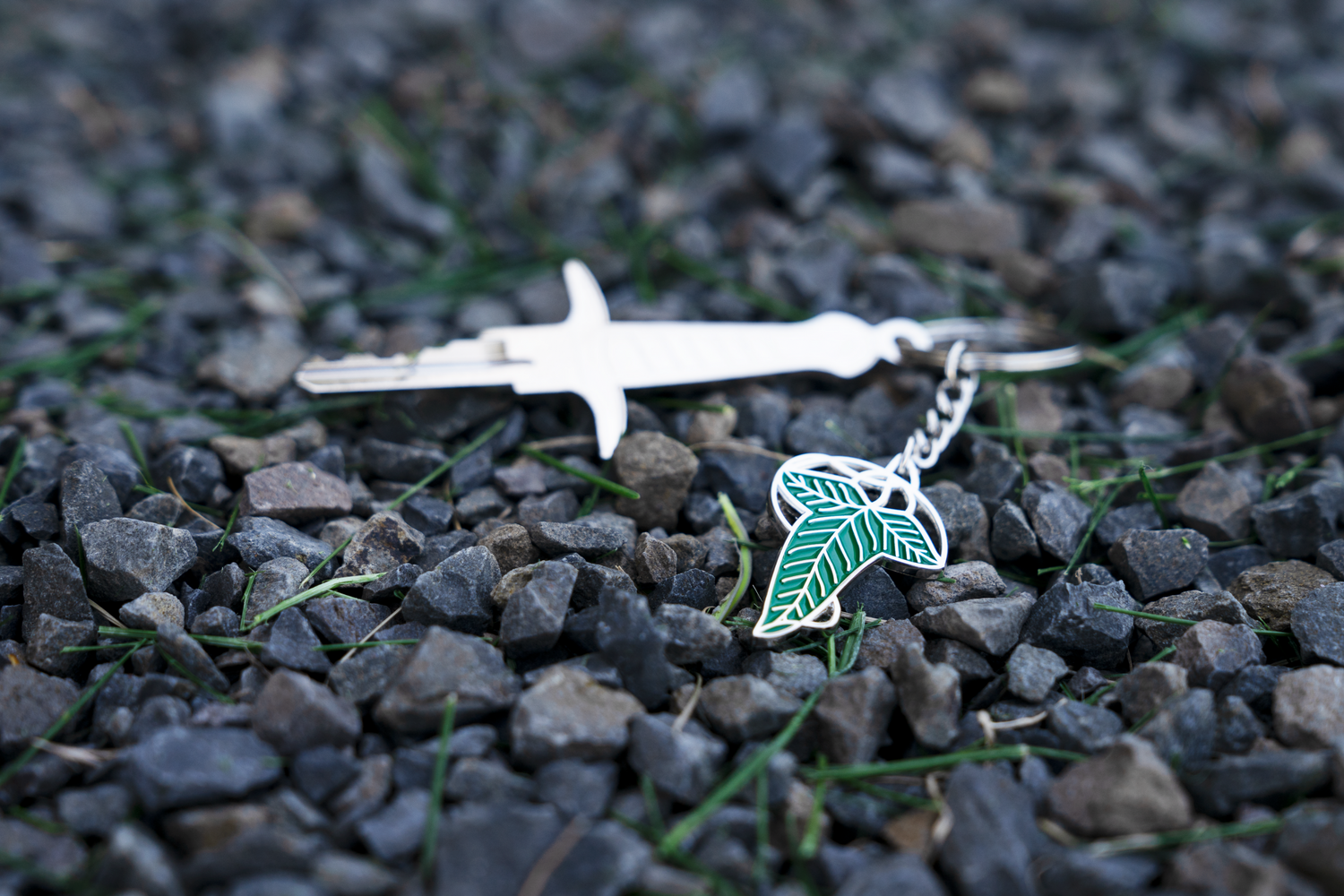 A silver house key attached to a green leaf keychain on top of a pile of pebbles