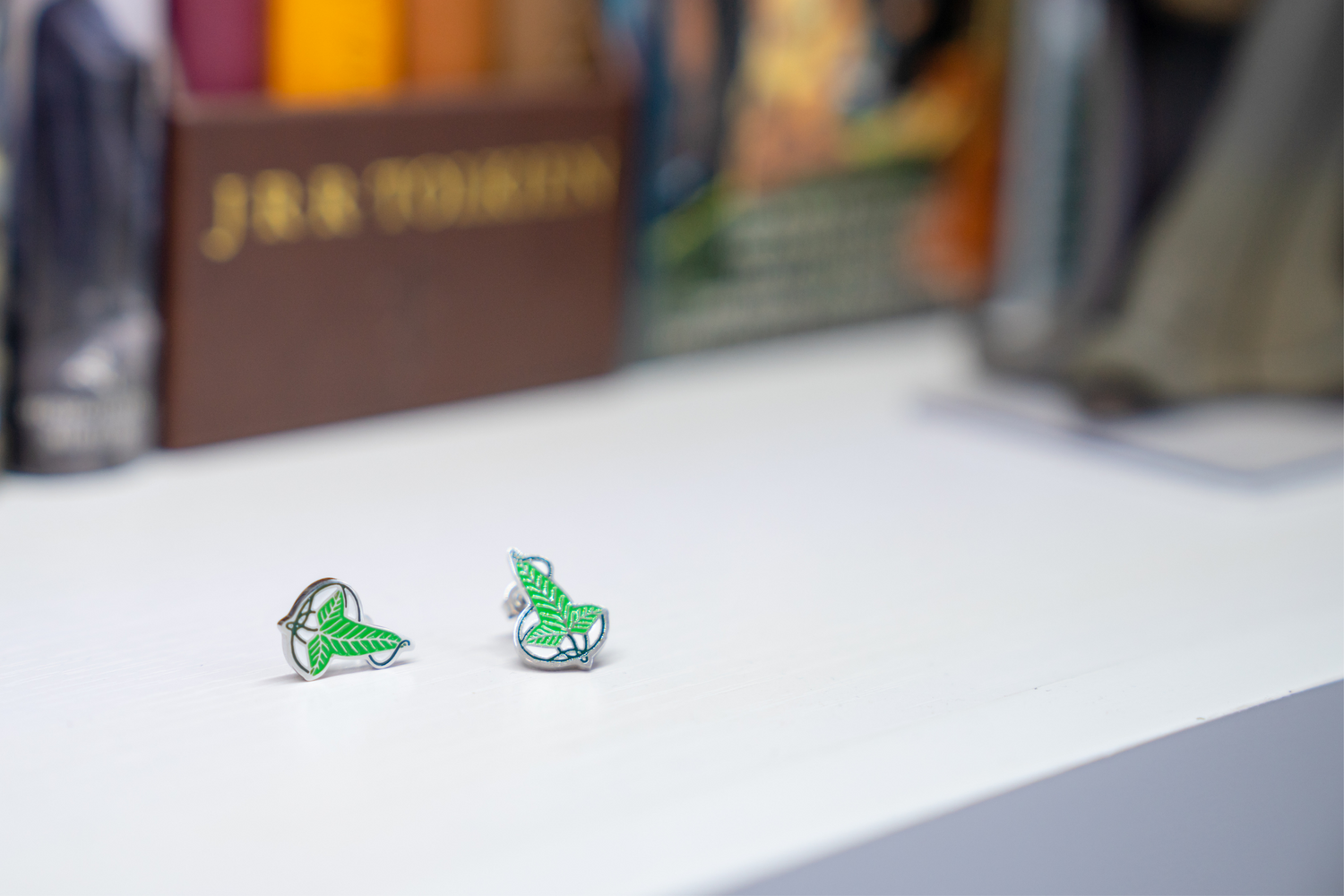 A pair of green earrings on a white bookshelf with several Lord of the Rings books in the background