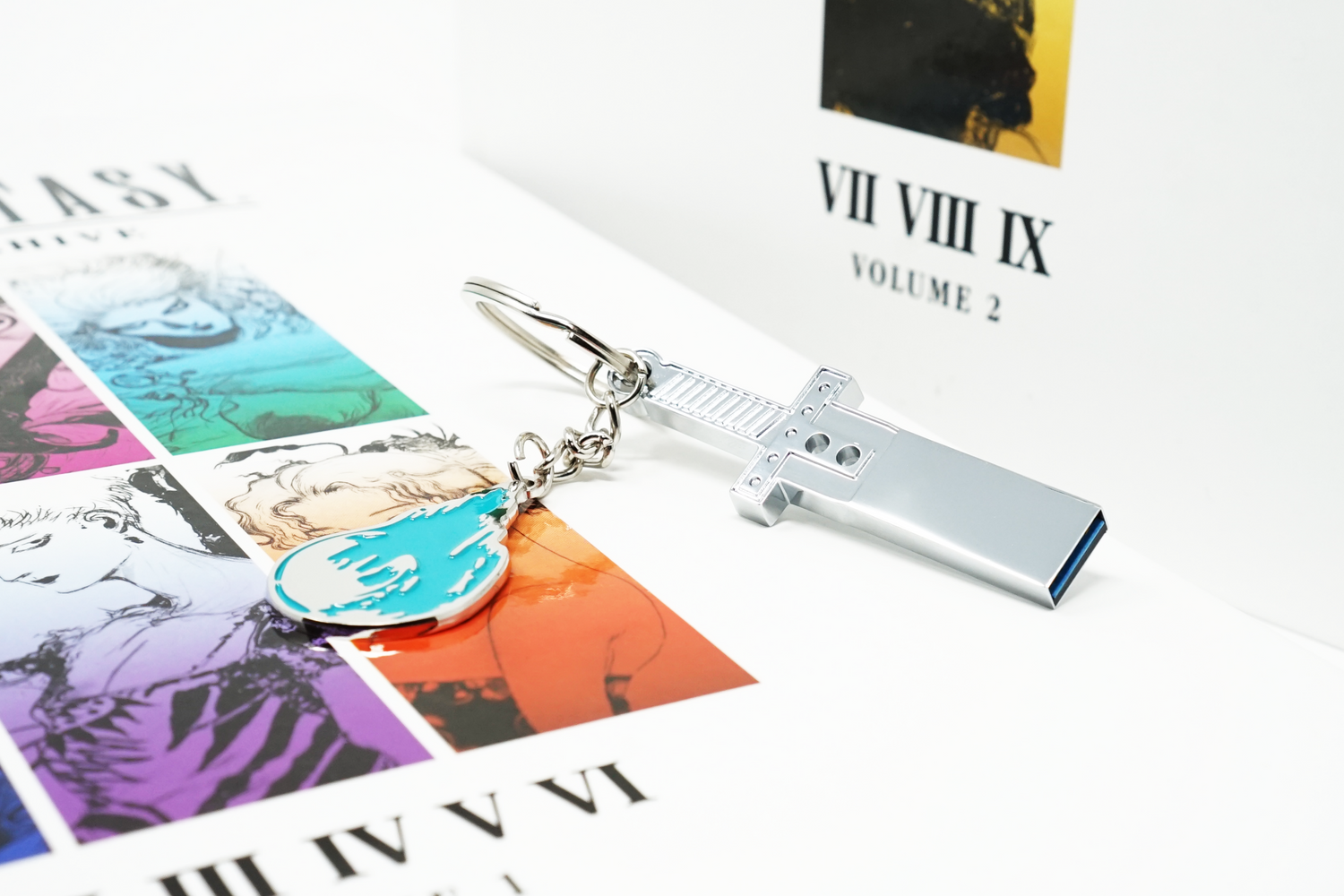 A silver USB drive and a cyan keychain on top of a variety of white books featuring art from Final Fantasy games