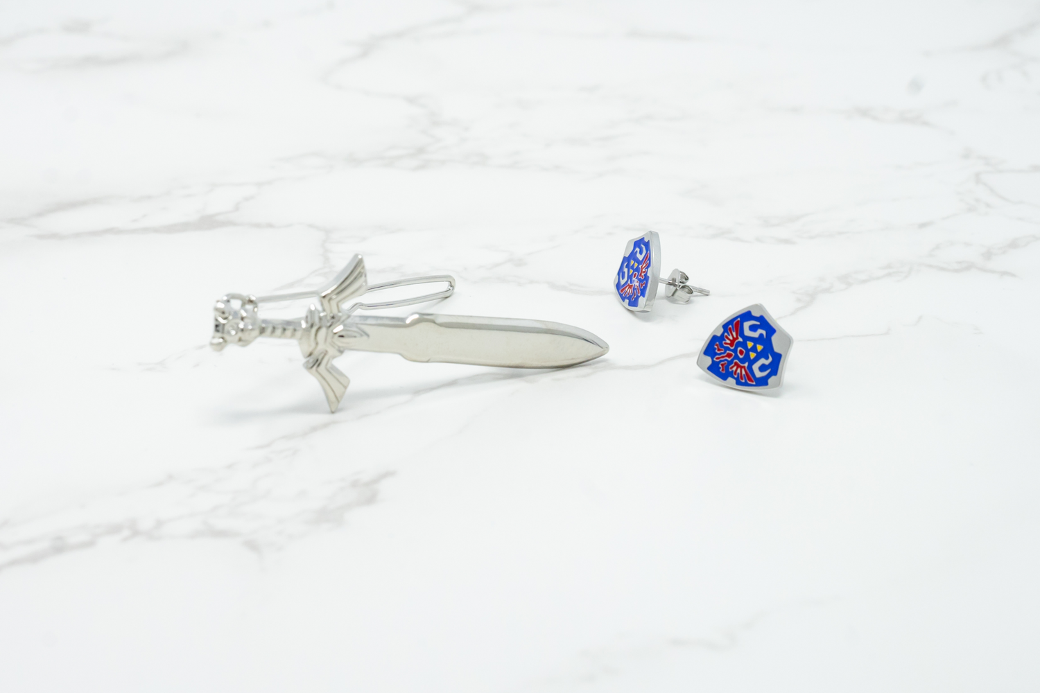 A silver hair clip next to a pair of blue, red and yellow earrings featuring a design inspired by the Legend of Zelda