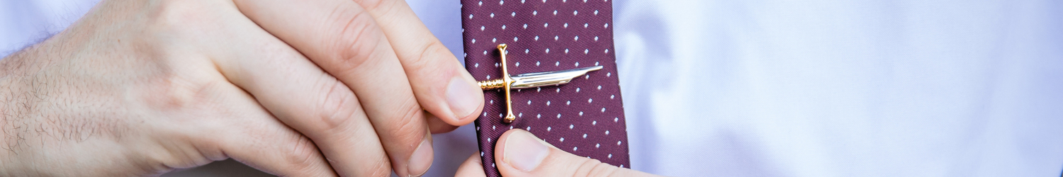 A gold and silver tie clip being clipped onto a read tie with a white shirt