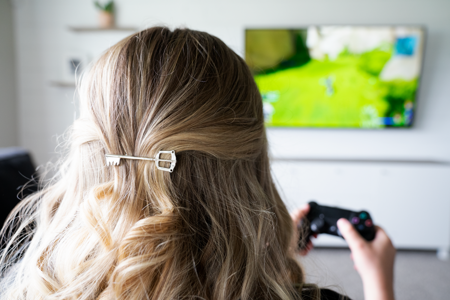 A silver hair clip on brown hair of a woman playing a Playstation 4