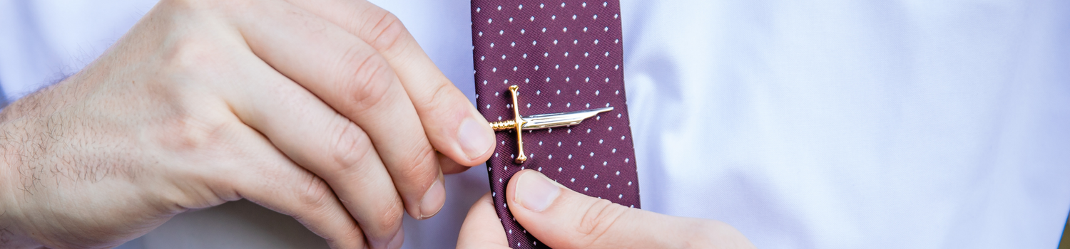 A silver and gold tie clip being clipped onto a red tie